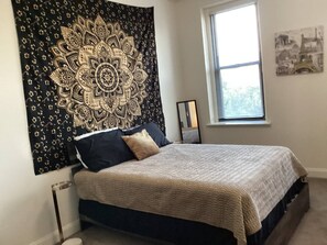 A bedroom with a bed, a tapestry, a window, and a painting on the wall. - The Downtown Hideaway – Stylish 1BR Comfort (Greensboro)