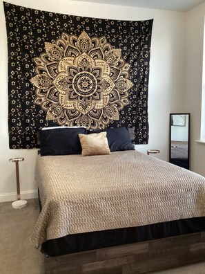 A bedroom with a bed, a large tapestry, and a bedside table. - The Downtown Hideaway – Stylish 1BR Comfort (Greensboro)