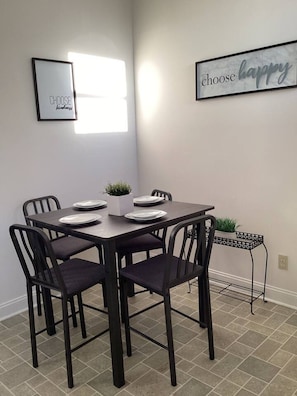 A dining area with a dark wooden table and chairs, a small potted plant, and two motivational wall art pieces. - The Downtown Hideaway – Stylish 1BR Comfort (Greensboro)