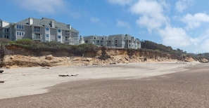 Une propriété située en bord de mer, comprenant plusieurs bâtiments à étages, une plage de sable et une falaise.