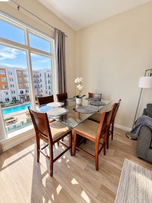 Zona pranzo moderna con tavolo in vetro e sedie di legno, vista su una piscina e sullo skyline urbano.