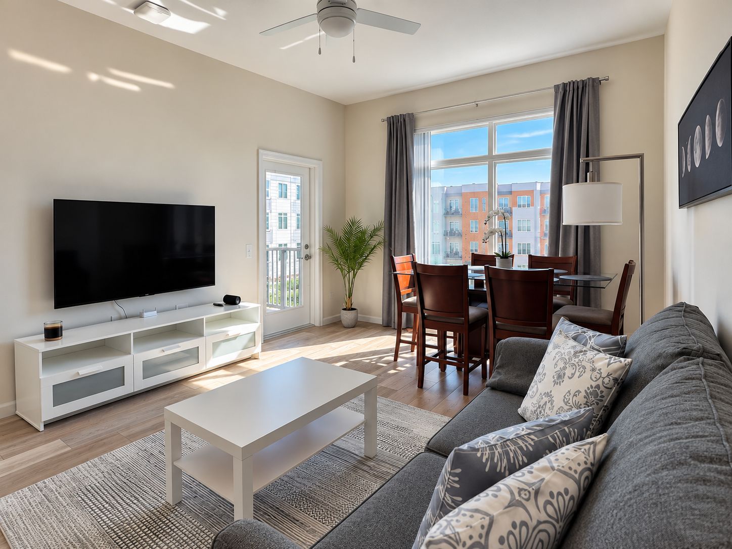 A modern living room with a flat-screen TV, a coffee table, a sofa, and a dining area with chairs and a table.