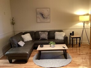 A living room with a sectional sofa, a coffee table, a floor lamp, and a wall-mounted abstract painting. - Downtown 2 Bedrooms: Walk to Everything (Greensboro)