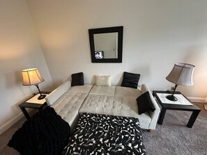A bedroom with a bed, two nightstands, a lamp, a mirror, and a patterned throw blanket. - Walkable Downtown King Bed Near Food and Nightlife (Greensboro)