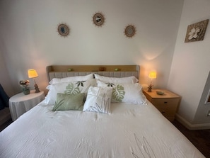 A neatly made bed with a headboard, two bedside tables with lamps, and wall decor. - Walkable Downtown King Bed Near Food and Nightlife (Greensboro)
