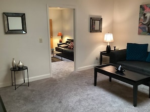 A living room with a sofa, coffee table, and a lamp. There is a picture frame on the wall and a vase on a side table. - Downtown Lounge Getaway with Two Living Spaces (Greensboro)