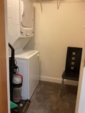 A laundry room with a washing machine, a dryer, a chair, and a vacuum cleaner. - Chic Cozy One Bedroom Walkable Downtown (Greensboro)