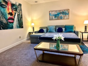 A hotel room with a sofa, a coffee table with a vase, two bedside tables with lamps, and artwork on the walls. - Chic Cozy One Bedroom Walkable Downtown (Greensboro)