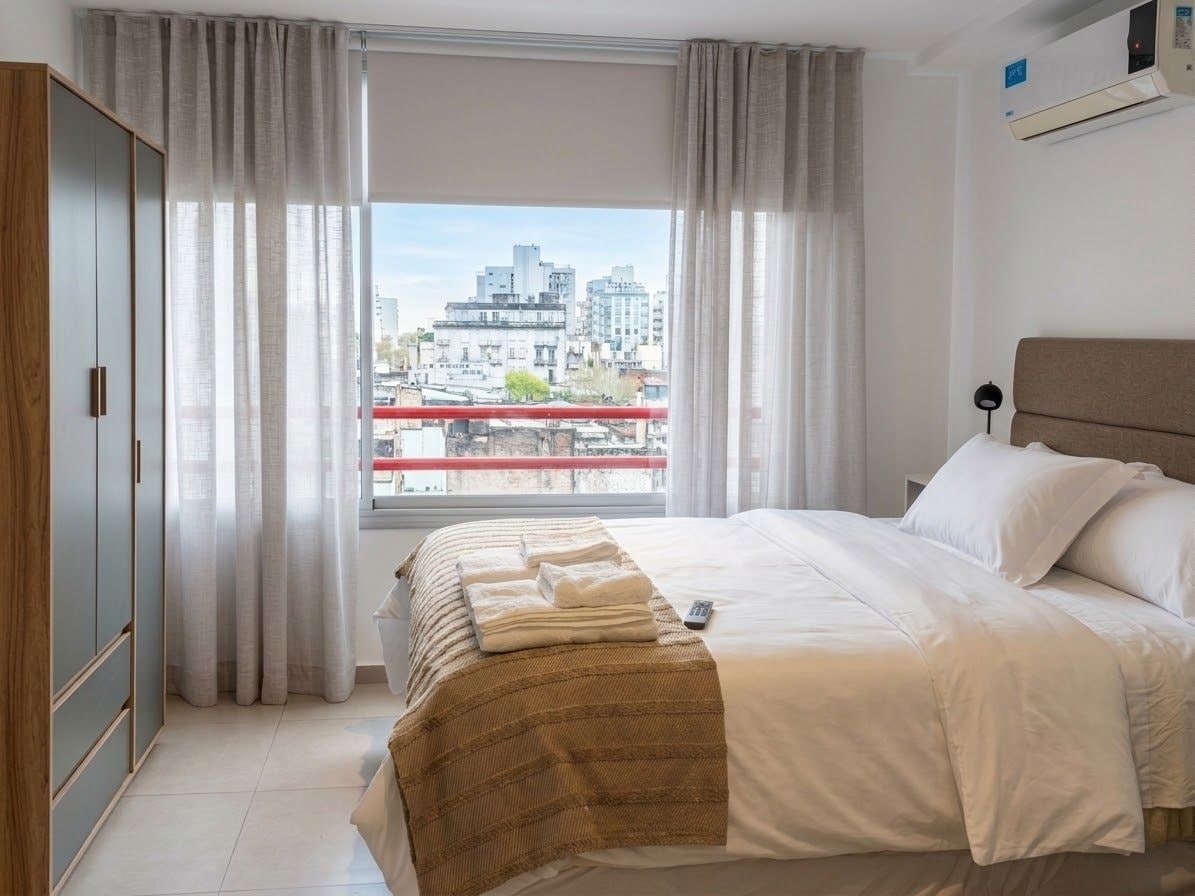 Una habitación de hotel con cama, cortinas, vista a la ciudad y aire acondicionado.