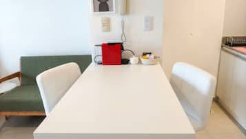 A modern, minimalist room with a white table, two white chairs, a green sofa, and a red bag on the table.