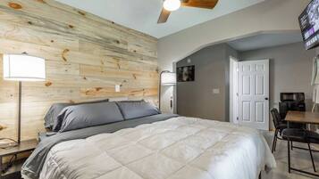 A bedroom with a bed, a ceiling fan, a desk with a chair, and a door.
