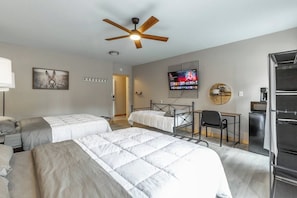 Ein Hotelzimmer mit zwei Betten, einem Schreibtisch, einem Sessel, einem Fernseher und einem Deckenventilator.
