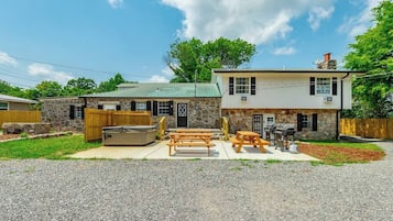 A two-story house with a stone exterior, a patio with picnic tables, and a barbecue grill.