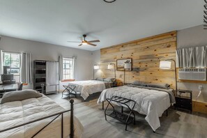 A room with two beds, a ceiling fan, a wooden wall panel, and a desk with a chair.