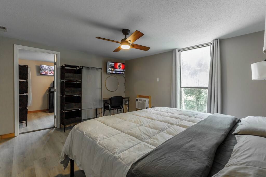 Un dormitorio con una cama, ventilador de techo, televisor y ventana.