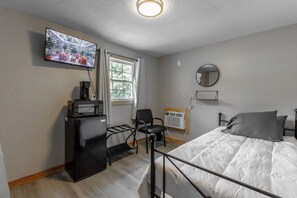 Ett sovrum med en säng, en tv som är monterad på väggen, ett skrivbord med en dator och ett fönster med gardiner.