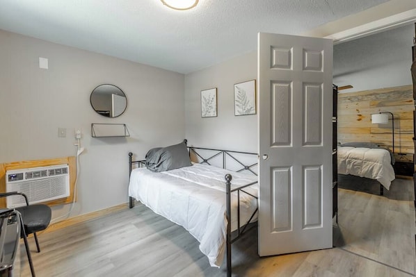 Un dormitorio con cama, mesita de noche, espejo y puerta que da a otra habitación.