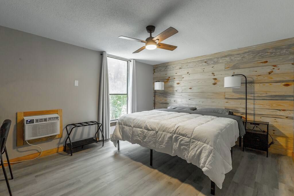 Un dormitorio con cama, ventilador de techo, radiador, ventana y una pared con diseño de paneles de madera.