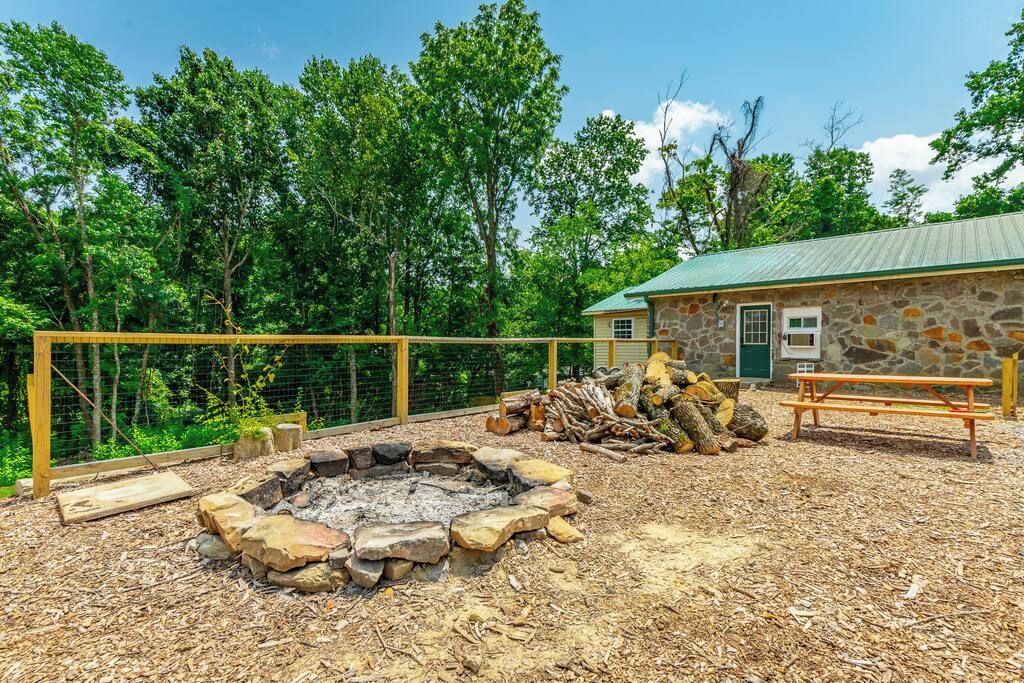 A stone building with a green roof, a fire pit surrounded by rocks, and a wooden fence.