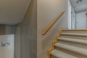 Een betegeld trappenhuis met een houten leuning en een witte deur op de achtergrond.