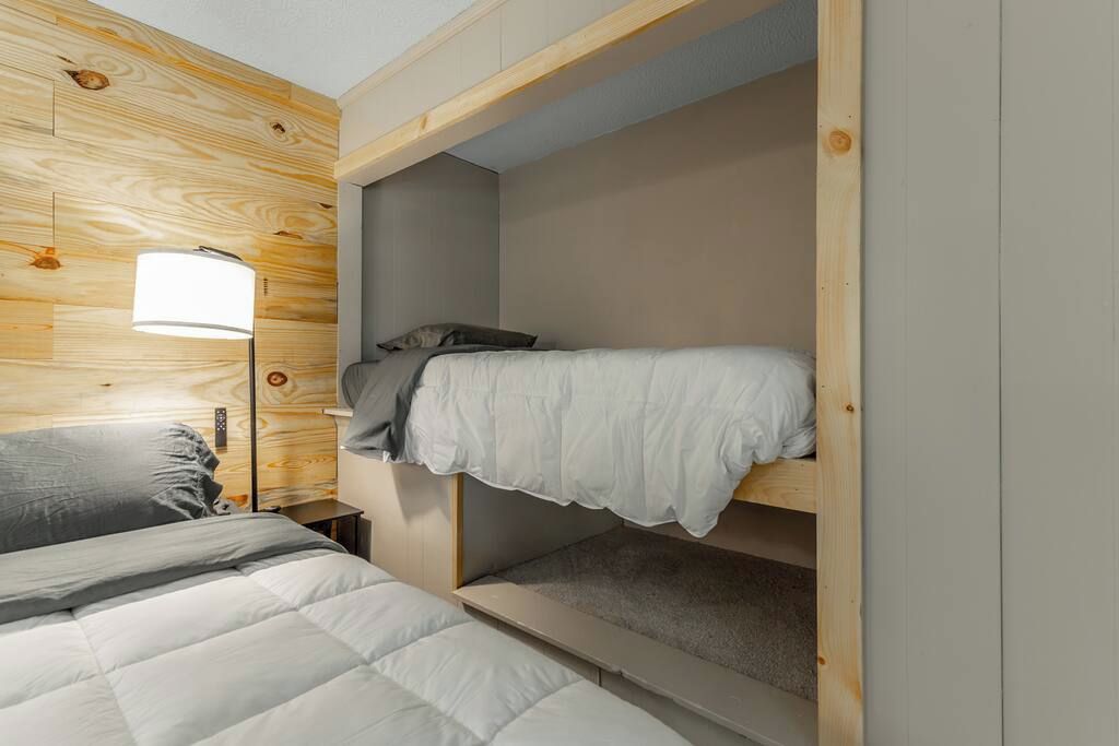 A bunk bed with a wooden headboard, a bedside table, and a lamp.