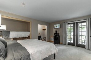 A bedroom with a bed, a TV, a desk, and a sliding door to a balcony.
