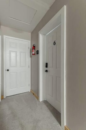 Un pasillo con dos puertas blancas, una de ellas con el número 6, y un extintor montado en la pared.