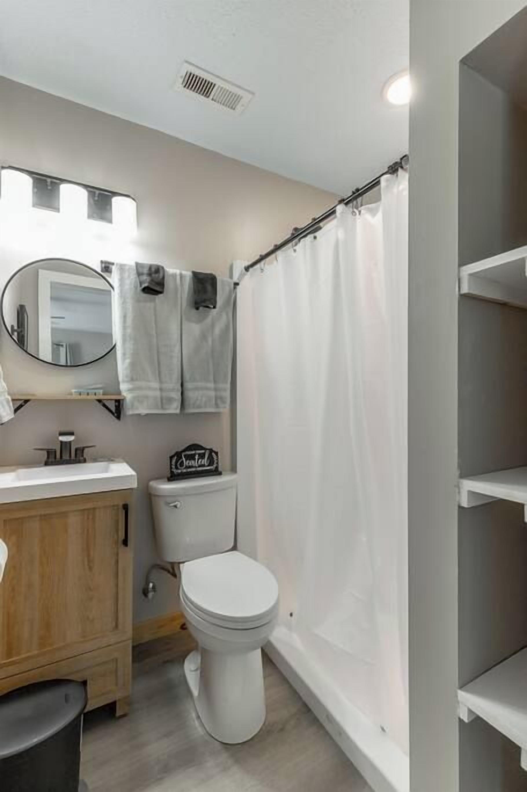 Baño con inodoro, lavamanos, espejo y cortina de ducha.