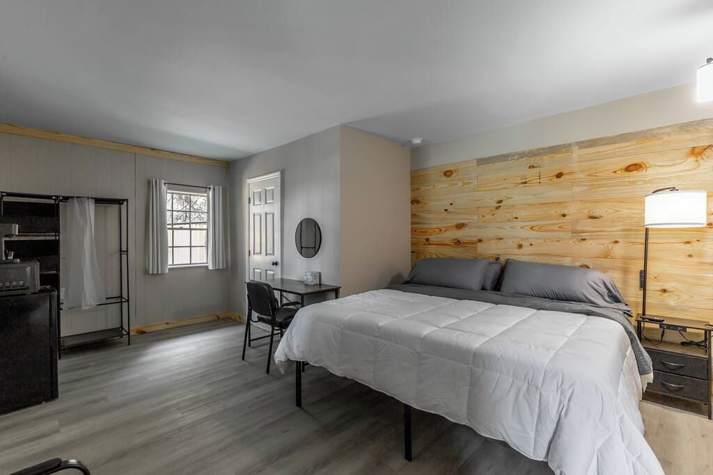 A bedroom with a bed, a desk, a chair, a wardrobe, and a wooden accent wall.