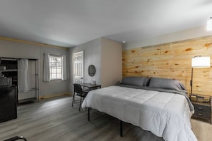 A bedroom with a bed, a desk, a chair, a wardrobe, and a wooden accent wall. - Wildflower Hotel on Lookout Mountain 7 (Rising Fawn)