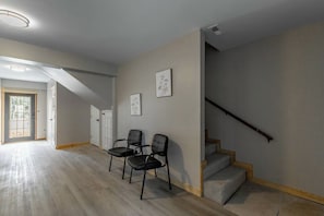 Un espacio interior con una escalera, dos sillas y una puerta que da a una zona luminosa.
