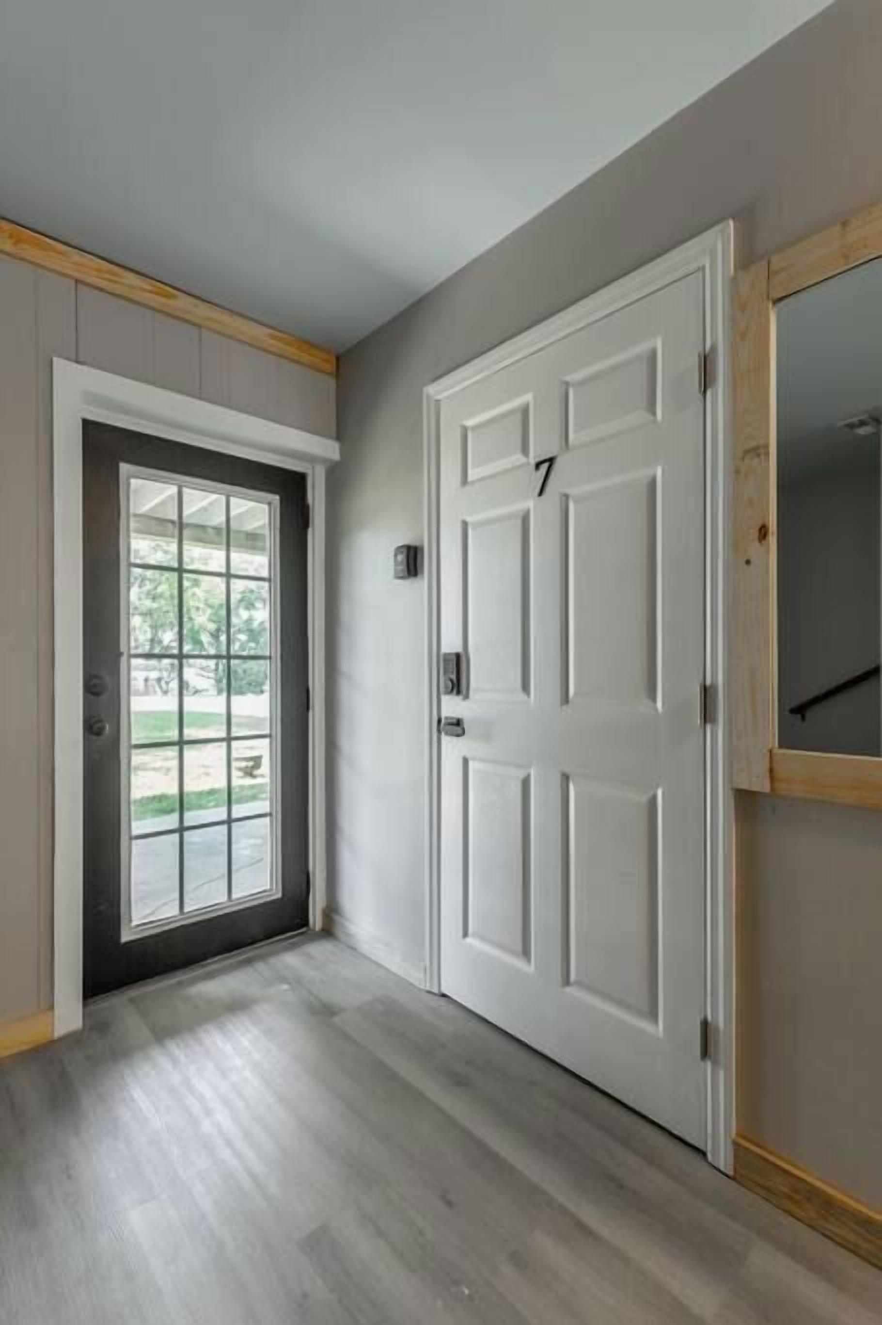 A hallway with a white door, a window, and a doorbell.