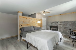 Ein Schlafzimmer mit einem Bett, einem Deckenventilator, einem Kamin aus Stein und einem Holzkopfteil.