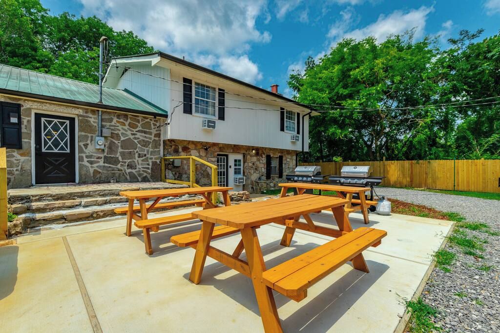 A stone building with a metal roof, a wooden deck with picnic tables, and a barbecue grill.