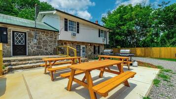 A stone building with a metal roof, a wooden deck with picnic tables, and a barbecue grill.