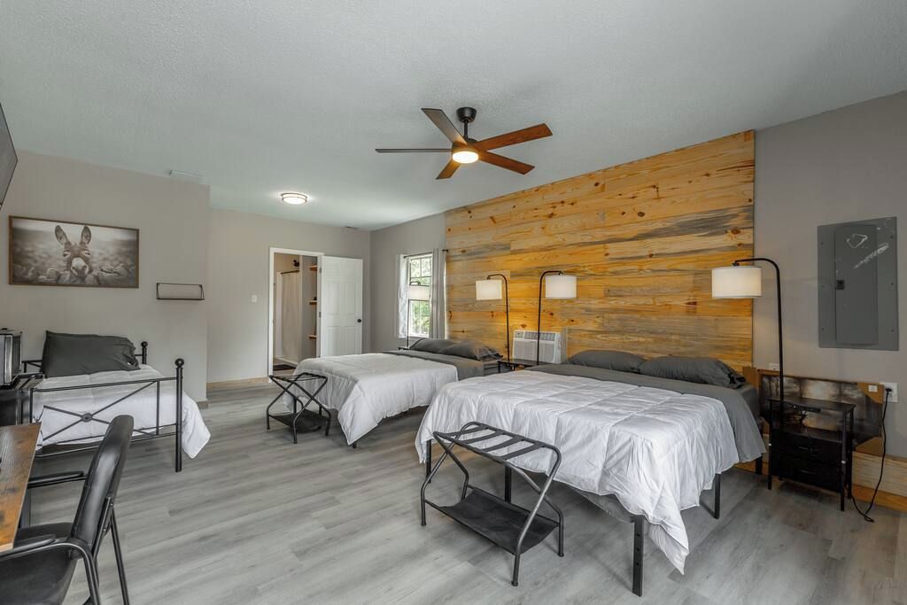 A hotel room with two beds, a ceiling fan, bedside lamps, a wooden accent wall, and a painting on the wall.