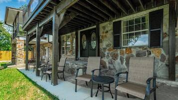 A covered outdoor seating area with stone walls and wooden beams, featuring several chairs and tables.