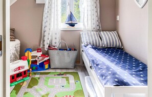 Ein Kinderzimmer mit einem Bett, einer Spieledecke, einem Spielzeug-Eisenbahnset und einem Ordnungskorb.