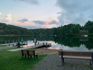Une vue sur le lac, avec un quai, des bancs et une maison en arrière-plan.