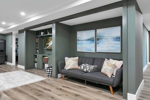 Un salon moderne avec un canapé gris, un tapis blanc et une bibliothèque.