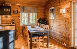 Ein Interieur einer Holzhütte mit Esstisch, Stühlen, einer Küchenzeile inklusive Herd und einem Fenster mit Blick auf Bäume.