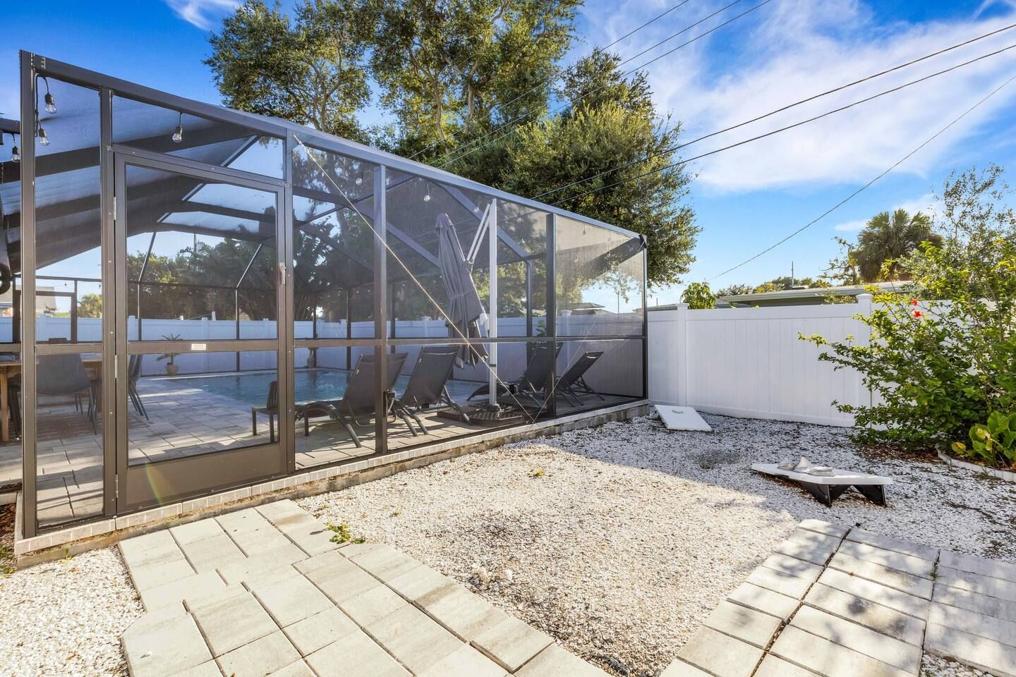 A modern outdoor pool area with a glass enclosure, lounge chairs, and a white fence.