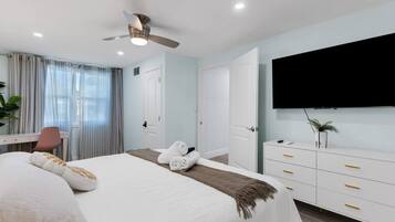 Quarto de hotel com cama, escrivaninha, cadeira, televisão e guarda-roupa.