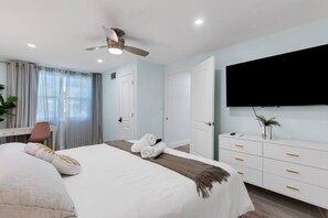 Quarto de hotel com cama, escrivaninha, cadeira, televisão e guarda-roupa.