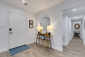 Um corredor com porta branca, mesa consola, luminárias, espelho e tapete azul.
