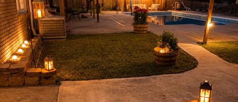 A backyard with a pool, outdoor seating, and decorative lighting.