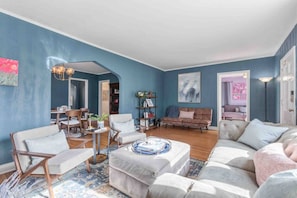 Un salon avec un mur bleu, un canapé, une table basse et un coin repas comprenant des chaises et une table.