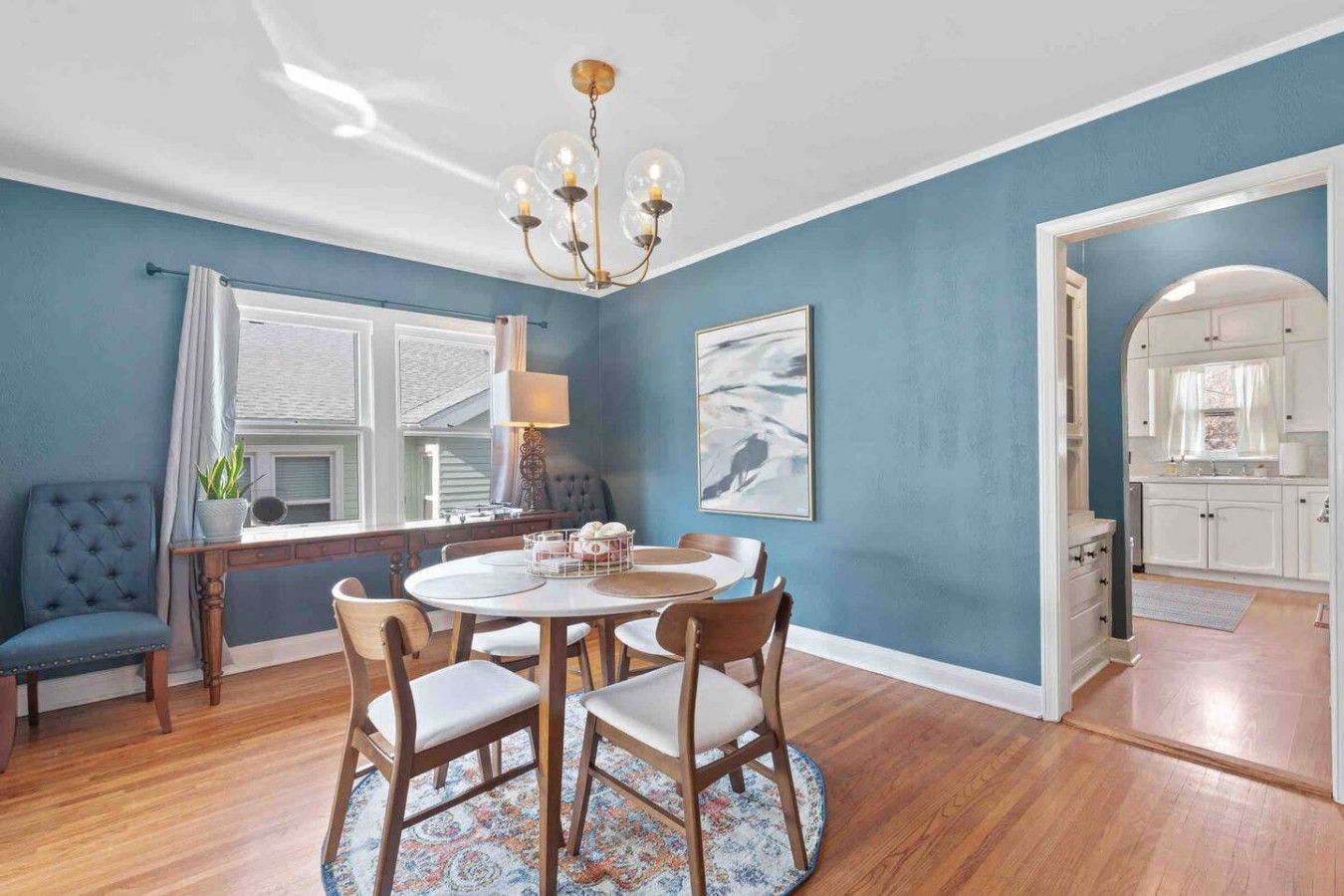 A dining area with a round table, chairs, a chandelier, and a view into the kitchen.