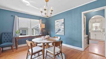 A dining area with a round table, chairs, a chandelier, and a view into the kitchen.