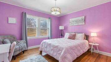 A bedroom with a bed, a desk, a chair, a window, and a lamp.